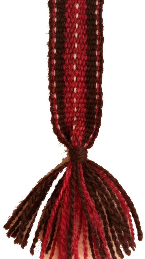 Närbild vävt förklädesband i cerise, mörkbrunt och gråvitt
